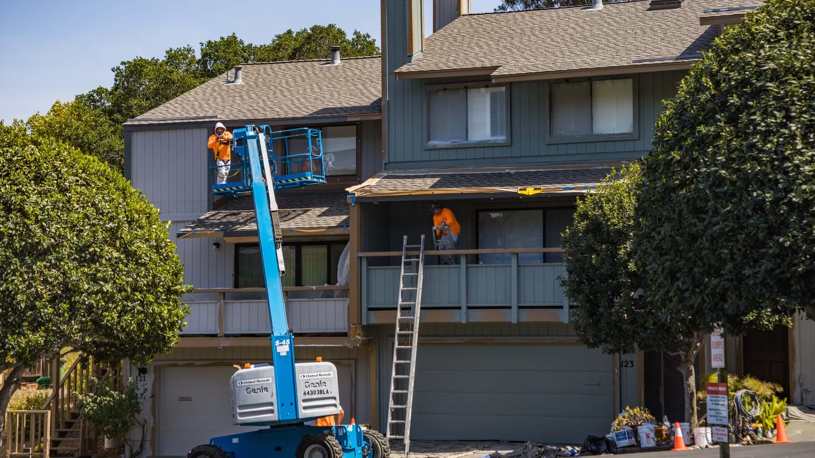 "Extension ladder leaning against a two-story suburban house, viewed from below, showing the height involved in cleaning second-story windows"